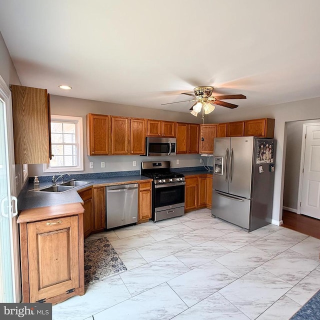 kitchen with brown cabinets, marble finish floor, a ceiling fan, a sink, and appliances with stainless steel finishes