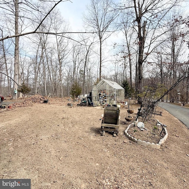 view of yard featuring an outbuilding, a greenhouse, and driveway