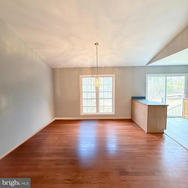 unfurnished dining area with baseboards, lofted ceiling, an inviting chandelier, and wood finished floors