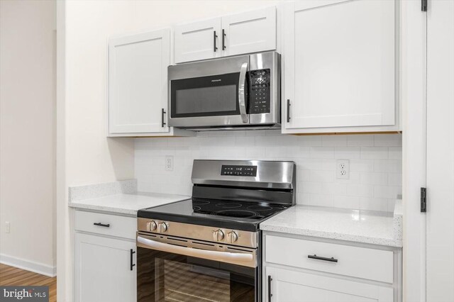 kitchen featuring white cabinetry, appliances with stainless steel finishes, light stone counters, and backsplash