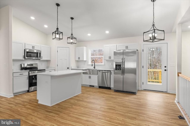 kitchen featuring stainless steel appliances, a kitchen island, white cabinets, and decorative light fixtures