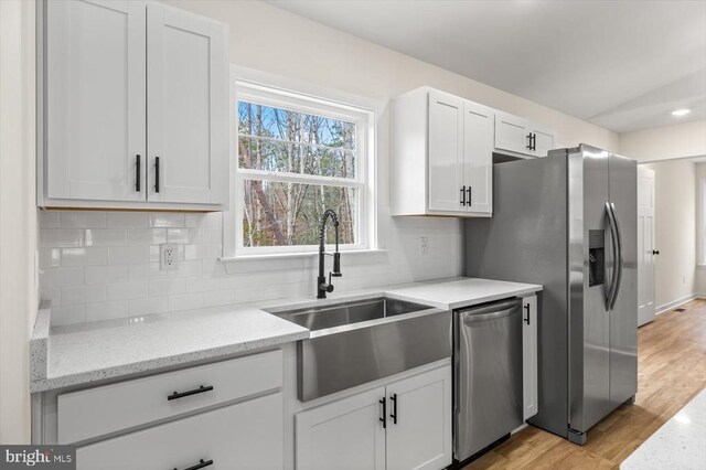 kitchen with appliances with stainless steel finishes, sink, white cabinets, light stone counters, and light wood-type flooring