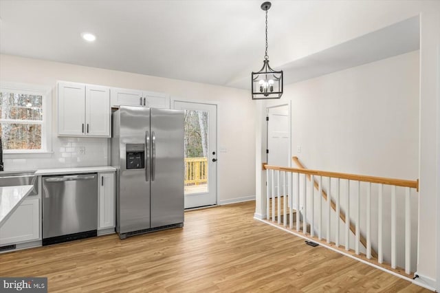 kitchen featuring white cabinetry, light wood-type flooring, pendant lighting, stainless steel appliances, and backsplash