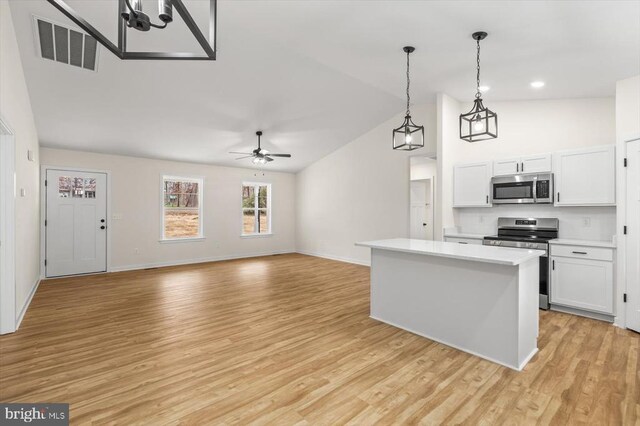 kitchen with appliances with stainless steel finishes, hanging light fixtures, light hardwood / wood-style floors, white cabinets, and a kitchen island