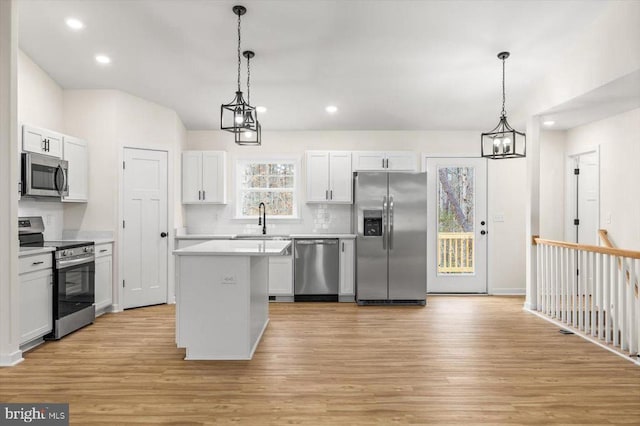 kitchen featuring sink, decorative light fixtures, a center island, stainless steel appliances, and white cabinets