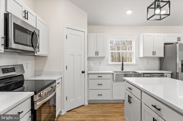 kitchen with sink, decorative light fixtures, light hardwood / wood-style flooring, appliances with stainless steel finishes, and white cabinets