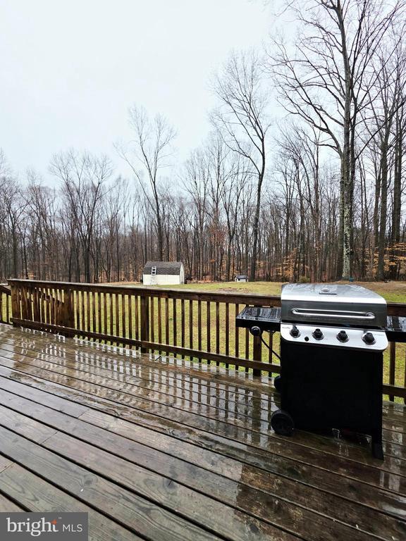 wooden deck featuring an outbuilding, a storage unit, a lawn, and a grill