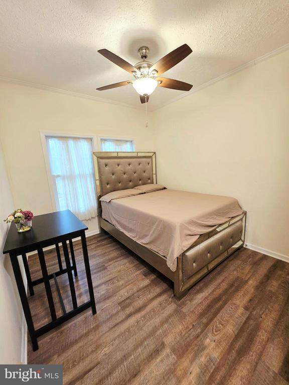 bedroom with crown molding, wood finished floors, baseboards, and a textured ceiling