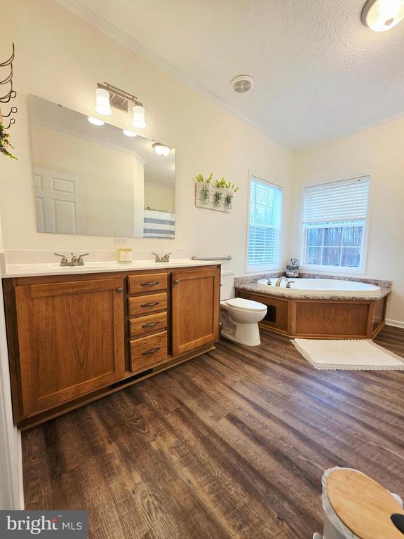 bathroom with toilet, double vanity, a bath, and wood finished floors