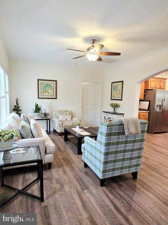 living room featuring a textured ceiling, crown molding, a ceiling fan, and wood finished floors