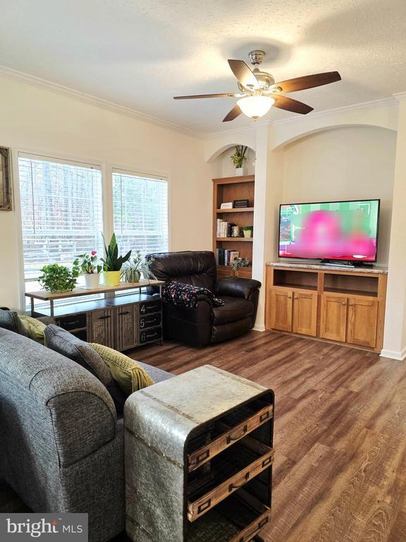 living area with ceiling fan, crown molding, wood finished floors, and a textured ceiling