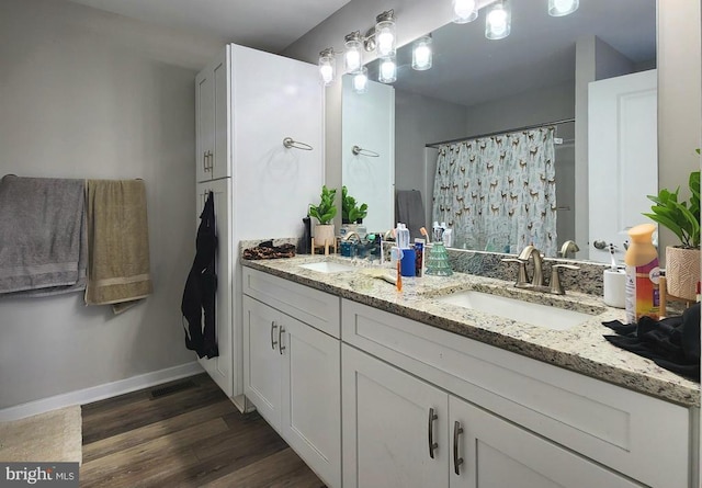 bathroom with a sink, double vanity, baseboards, curtained shower, and wood finished floors
