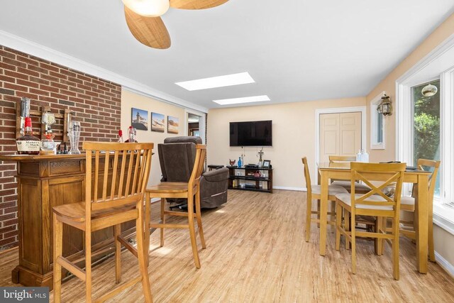 dining area with crown molding, ceiling fan, brick wall, and light wood-type flooring