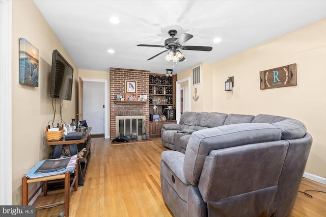 living room with ceiling fan, a fireplace, and light hardwood / wood-style floors