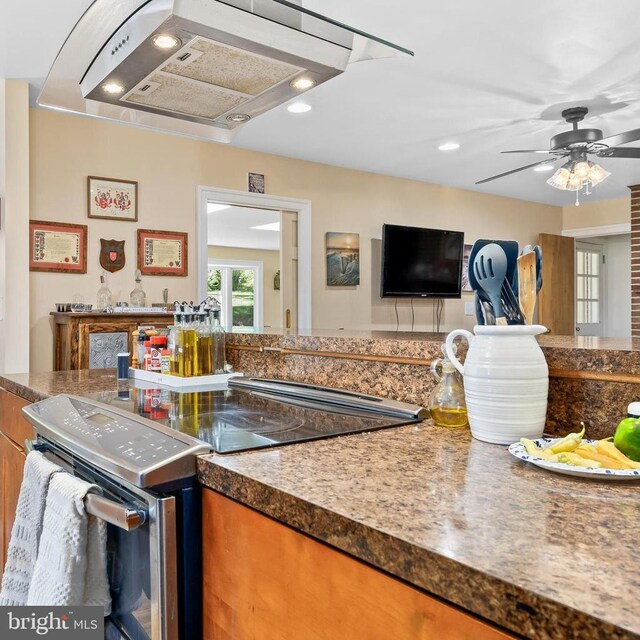 kitchen featuring wall chimney range hood, stainless steel range with electric cooktop, and ceiling fan