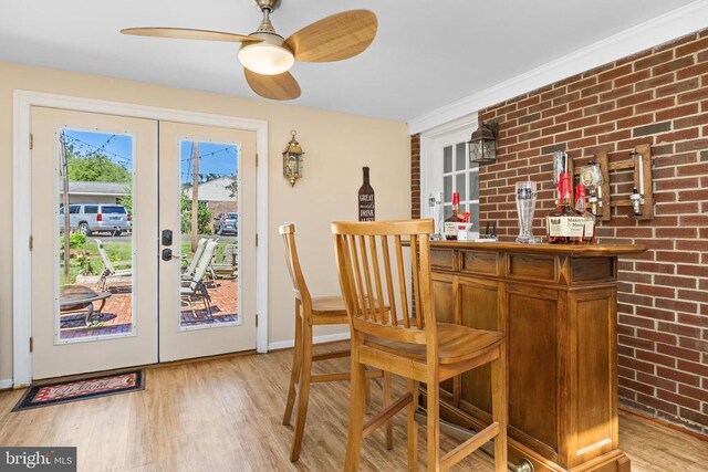 bar featuring ceiling fan, brick wall, light wood-type flooring, and french doors