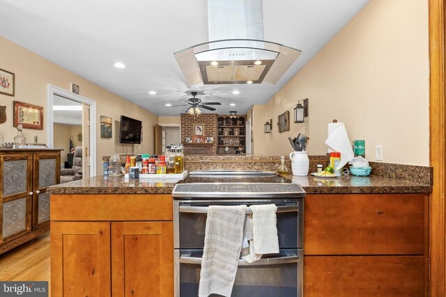 kitchen featuring light hardwood / wood-style flooring, ceiling fan, double oven range, island range hood, and kitchen peninsula