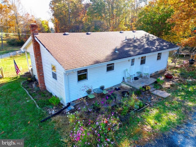 rear view of house featuring a lawn, a chimney, a shingled roof, and entry steps