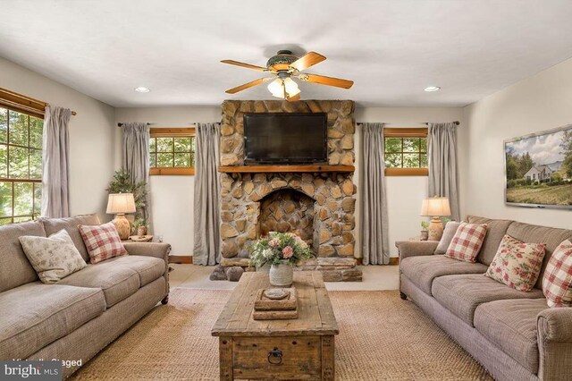 living room featuring a stone fireplace, a wealth of natural light, and ceiling fan