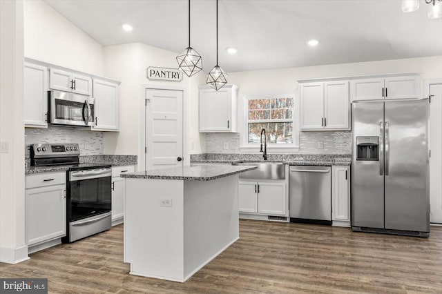 kitchen featuring a kitchen island, appliances with stainless steel finishes, decorative light fixtures, sink, and white cabinets