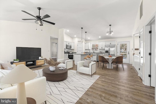 living room with vaulted ceiling, ceiling fan with notable chandelier, and light hardwood / wood-style flooring