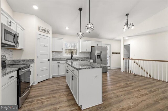 kitchen with a kitchen island, appliances with stainless steel finishes, white cabinetry, sink, and dark stone counters