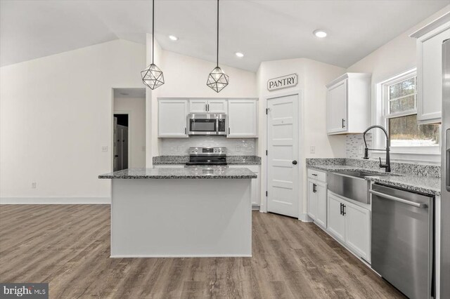 kitchen featuring a kitchen island, appliances with stainless steel finishes, decorative light fixtures, white cabinets, and light stone countertops