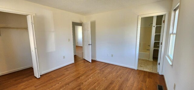 unfurnished bedroom with ensuite bathroom, hardwood / wood-style floors, a textured ceiling, and a closet