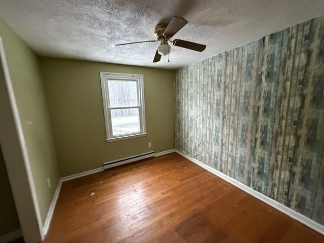 spare room featuring a textured ceiling, baseboards, baseboard heating, and wood finished floors