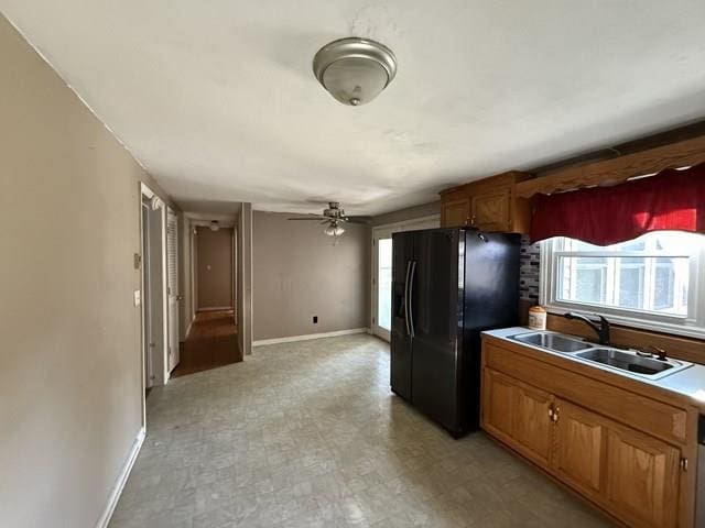 kitchen with brown cabinets, light floors, light countertops, freestanding refrigerator, and a sink