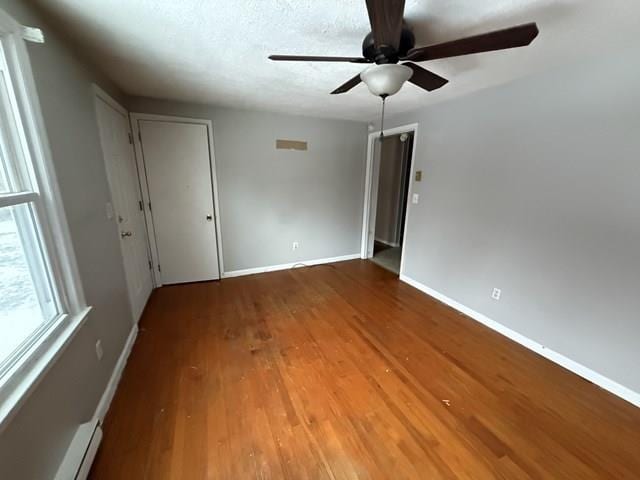 unfurnished room with a baseboard heating unit, ceiling fan, wood finished floors, and baseboards