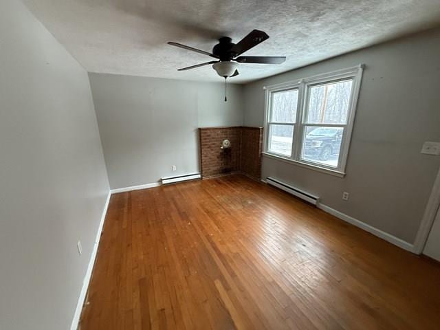 interior space featuring a textured ceiling, baseboard heating, hardwood / wood-style flooring, and baseboards