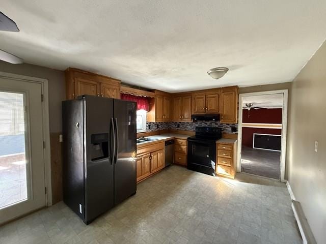 kitchen featuring brown cabinetry, light floors, light countertops, black appliances, and exhaust hood