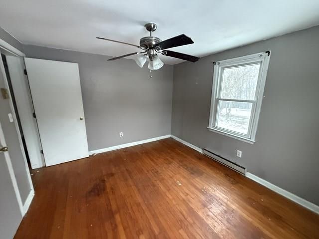 unfurnished bedroom with a baseboard heating unit, wood finished floors, a ceiling fan, and baseboards