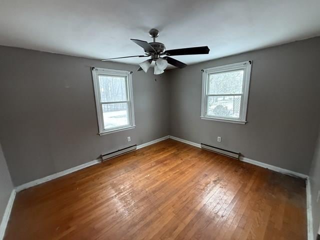 unfurnished room with wood-type flooring, baseboard heating, and a wealth of natural light