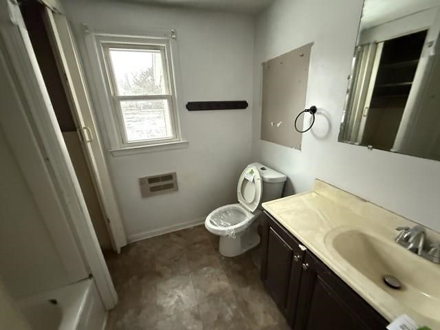 bathroom featuring baseboards, a wall unit AC, toilet, a bathtub, and vanity