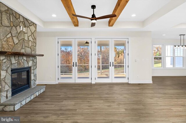 unfurnished living room with a stone fireplace, hardwood / wood-style floors, ceiling fan, beam ceiling, and french doors