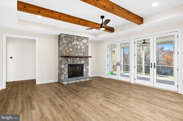 unfurnished living room with french doors, wood-type flooring, beamed ceiling, ceiling fan, and a fireplace