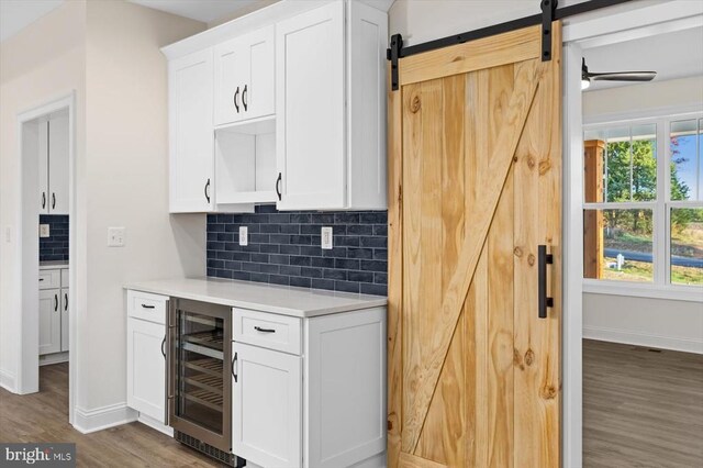 kitchen featuring tasteful backsplash, white cabinets, a barn door, dark hardwood / wood-style flooring, and beverage cooler