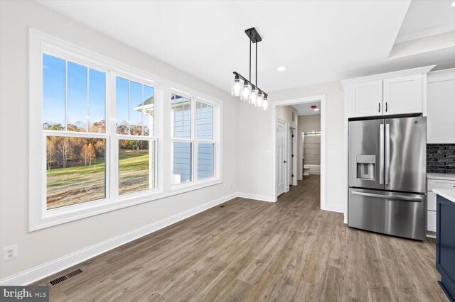 kitchen with pendant lighting, tasteful backsplash, white cabinetry, stainless steel fridge, and light wood-type flooring