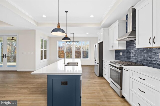 kitchen with a raised ceiling, sink, a kitchen island with sink, and wall chimney range hood