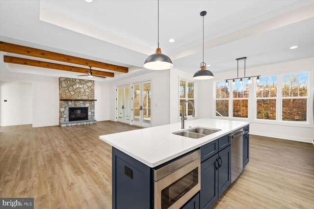 kitchen with sink, a center island with sink, light wood-type flooring, pendant lighting, and stainless steel appliances