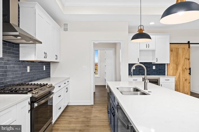 kitchen with sink, wall chimney range hood, white cabinetry, gas stove, and a barn door