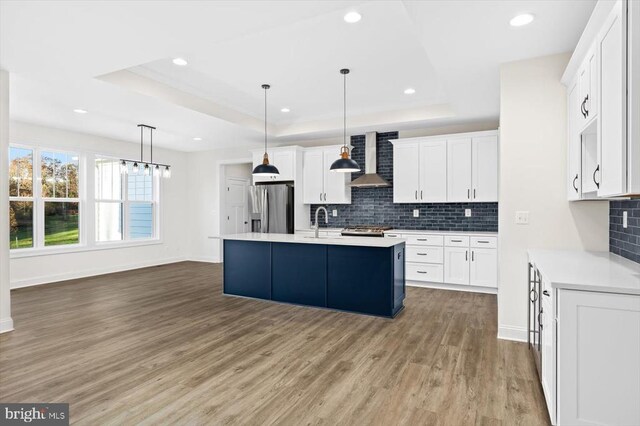 kitchen with stainless steel refrigerator with ice dispenser, a raised ceiling, an island with sink, pendant lighting, and white cabinets