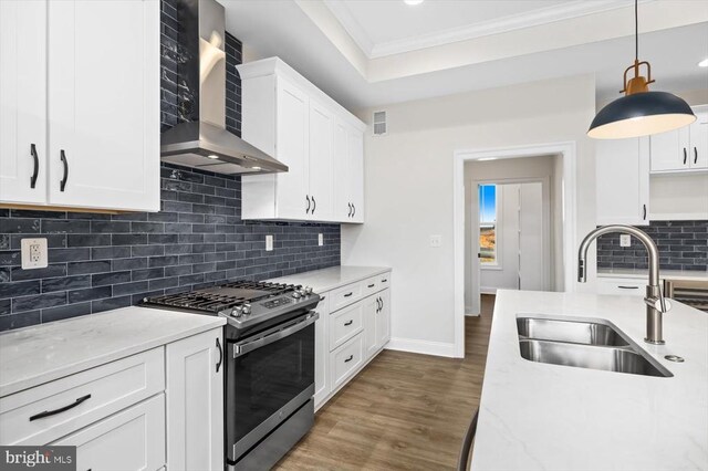 kitchen featuring pendant lighting, sink, white cabinets, gas range, and wall chimney exhaust hood