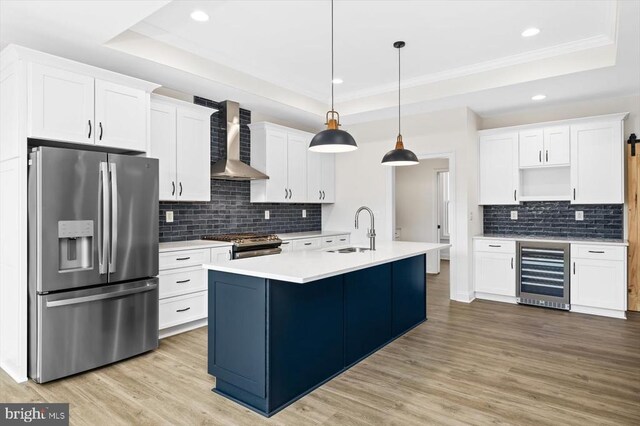 kitchen with decorative light fixtures, appliances with stainless steel finishes, a raised ceiling, beverage cooler, and wall chimney range hood