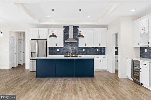 kitchen with pendant lighting, a tray ceiling, stainless steel fridge, and wall chimney exhaust hood