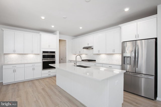 kitchen featuring sink, a kitchen island with sink, stainless steel appliances, light hardwood / wood-style floors, and white cabinets