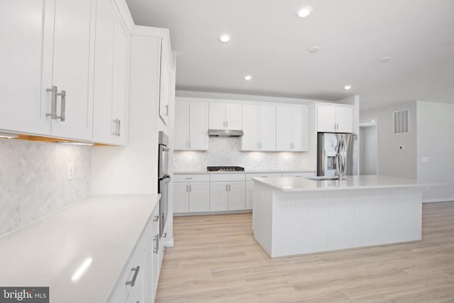 kitchen featuring tasteful backsplash, white cabinets, a center island with sink, stainless steel fridge with ice dispenser, and light wood-type flooring