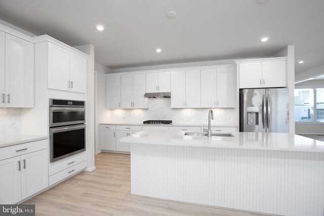 kitchen featuring white cabinetry, sink, decorative backsplash, a kitchen island with sink, and stainless steel appliances